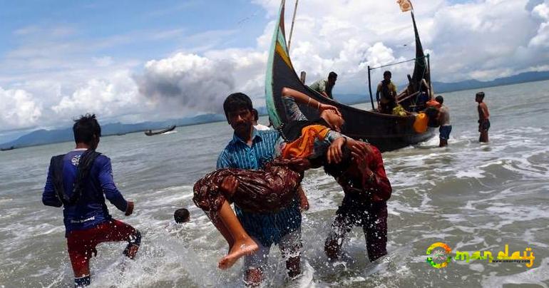 Smoke is seen on Myanmar’s side of border as an exhausted Rohingya refugee woman is carried to the shore after crossing the Bangladesh-Myanmar border by boat through the Bay of Bengal